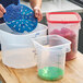 A set of translucent round polypropylene food storage containers with measurement markings and colored inserts, including one container filled with strawberries and a red lid.