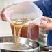 A translucent round polypropylene food storage container being used to pour liquid.