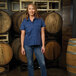 A women's navy blue short sleeve work shirt paired with jeans, modeled in front of stacked wooden barrels.