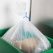 A clear plastic bag secured with a blue twist tie inside a green bin.