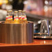 A rose gold stainless steel party tub holding several bottled beverages on a bar counter.