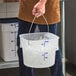 A translucent 12-quart round food storage pail with a bail handle, partially filled with ice.