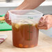 A translucent 4-quart round polypropylene food storage container with measurement markings, filled with liquid and vegetables.