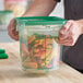 A translucent 4-quart round polypropylene food storage container with a green lid, filled with cut vegetables.