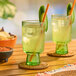 A glass of cucumber agua fresca with ice, a straw, and a cucumber slice garnish on a wooden table.