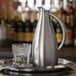 A brushed stainless steel pitcher and a glass of ice water on a metal tray.