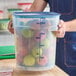 A large translucent round plastic food storage container with a blue lid, filled with apples.