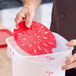 A red round plastic drain tray being placed into a clear food storage container.