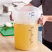 A large translucent round polypropylene food storage container with blue measurement markings, filled with liquid and held by a person.