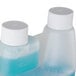 A plastic bottle of Urnex Rinza milk frother cleaner with blue liquid inside and white caps.