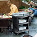 A Rubbermaid black plastic bussing cart with containers of food on it.