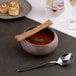 A round gold and brown porcelain bowl filled with soup, garnished with breadsticks and a mint leaf.