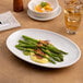 An oval, rimless warm white porcelain coupe plate displayed with food on a table.