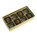 An 8-cavity gold candy box with a transparent lid, containing four round chocolates.