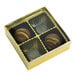 A gold 4-cavity candy box with a transparent lid, containing two chocolate candies.