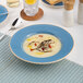 A blue round wide rim deep porcelain plate with soup, measuring 10 1/4 inches in diameter.