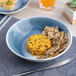 A round blue and white ombre porcelain deep coupe plate holding a cheese spread and seed crackers.