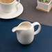 A small white porcelain creamer with a handle and spout, filled with cream.