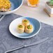 A blue and white ombre slanted porcelain flat coupe plate holding three small puff pastry appetizers.