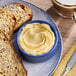 A blue ramekin filled with a swirl of European-style salted butter blend margarine, served on a plate with slices of multigrain bread.