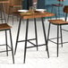 A square bar-height table with a wooden top and black metal legs.