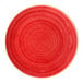 A round, rimless red porcelain plate with a twister pattern.