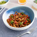 A large round porcelain coupe bowl with a blue and white ombre design, filled with noodles, broccoli, and red bell peppers.
