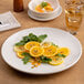 A large, round, warm white porcelain rimless coupe plate displaying a citrus and greens salad.