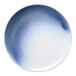 A round porcelain flat coupe plate with a blue and white ombre design and subtle speckled accents.