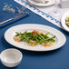 An oval white porcelain platter with an embossed wide rim, shown holding a serving of asparagus and garnishes.