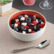 A round porcelain bowl with a red interior and white exterior, filled with assorted berries and small cheese cubes.