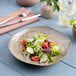 A gold and brown irregular round porcelain deep plate with a salad served on it.