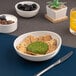 A white porcelain slanted coupe bowl filled with crackers and a green herb-coated cheese ball.