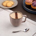 A gold and brown porcelain cup filled with a frothy beverage, placed on a table with a spoon nearby.