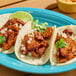 A plate of three tacos filled with chopped pork al pastor, garnished with onions and cilantro, served with a lime wedge.