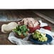 A serving of shredded pork carnitas in a red bowl, accompanied by tortillas, fresh cilantro, and tomatillos on a plate.