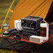 A portable power station and extra battery set up on a camping table with various electronic devices connected.