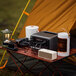 A portable power station, the EcoFlow RIVER 3 Plus, is placed on a camping table alongside various electronic devices and camping gear.