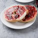 A white porcelain plate holding a sliced bagel with jam spread on top.