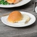 A small round white porcelain plate with a wide rim, holding a dinner roll and a portion of butter.