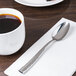A stainless steel teaspoon with a textured handle placed on a white napkin next to a cup of coffee.