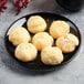 A black porcelain coupe plate holding seven cream puffs.