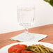 A clear glass goblet filled with water, placed on a white napkin next to a plate of food on a wooden table.