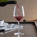 A clear wine glass with pour control markings being filled with red wine.
