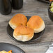 A small black porcelain coupe plate holding three bread rolls.