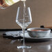 A clear stemmed wine glass with pour control markings being filled with white wine.