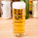 A clear Libbey 16 oz. specialty cooler glass filled with light beer and topped with foam.