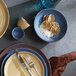 A blue terracotta salad bowl filled with dried citrus slices and coarse salt, shown alongside matching dinnerware.