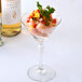 A clear 6 oz. martini glass filled with shrimp cocktail and garnished with herbs.