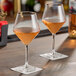 A pair of clear, stemmed wine glasses partially filled with rosÃ© wine, placed on square coasters on a bar surface.